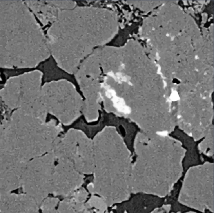 Grayscale image of irregular light-gray particles separated by dark gaps, with a bright white patch center-right